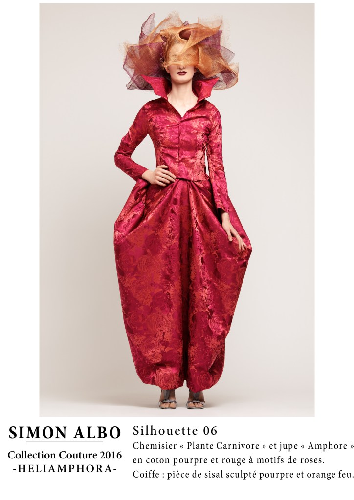 Simon Albo, créateur couture : chemisier rouge et jupe pourpre avec motifs floraux, coiffe sisal pourpre et orange feu, silhouette couture et mode artistique.